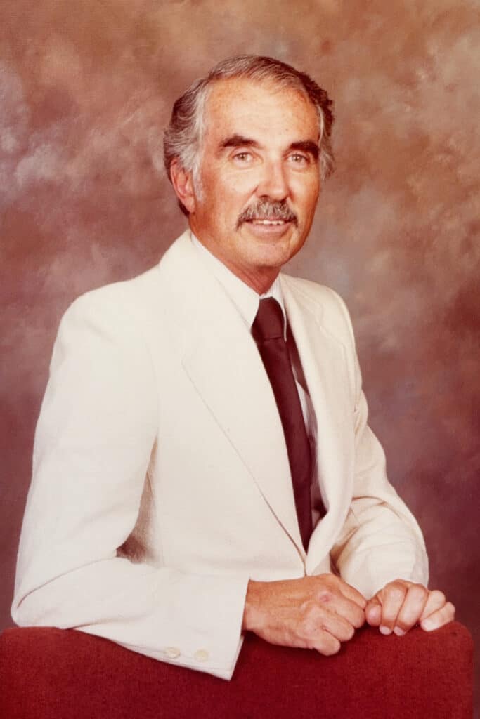 A red-tinted portrait of Rudolph Cutino from the bust up. He is wearing a white suit and a red tie.